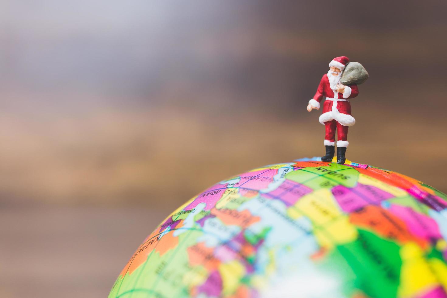 Miniature Santa Claus carrying gifts standing on a globe photo