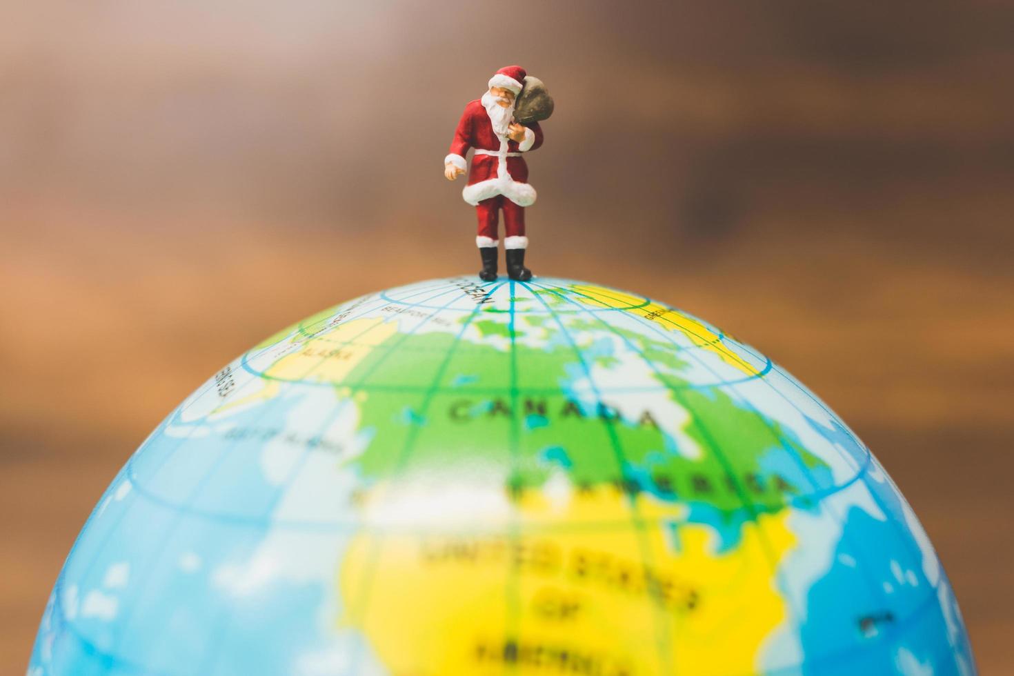 Miniature Santa Claus carrying gifts standing on a globe photo