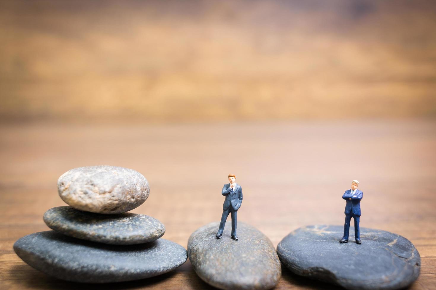 Miniature businessmen standing on a stone, challenges and risks concept photo