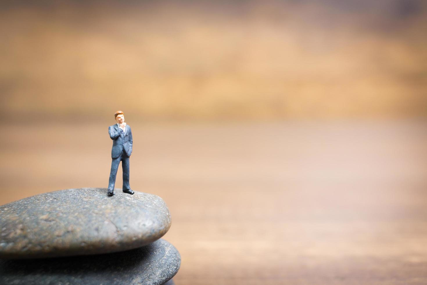 Empresario en miniatura de pie sobre una piedra, concepto de desafíos y riesgos foto