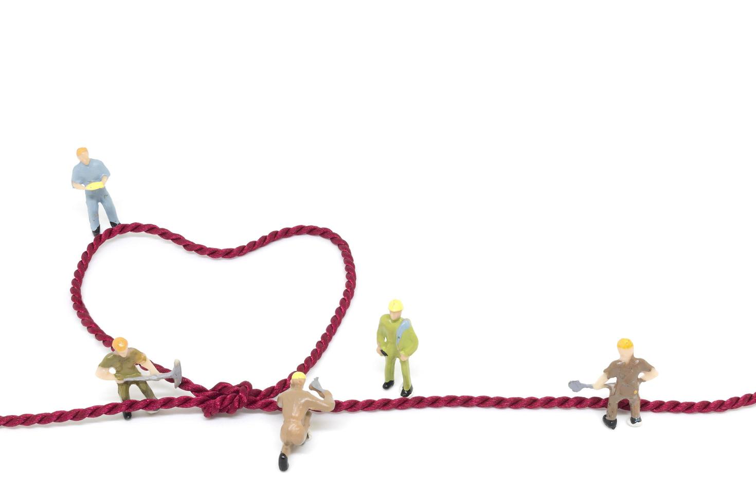 Miniature workers building a heart-shaped rope on a white background photo