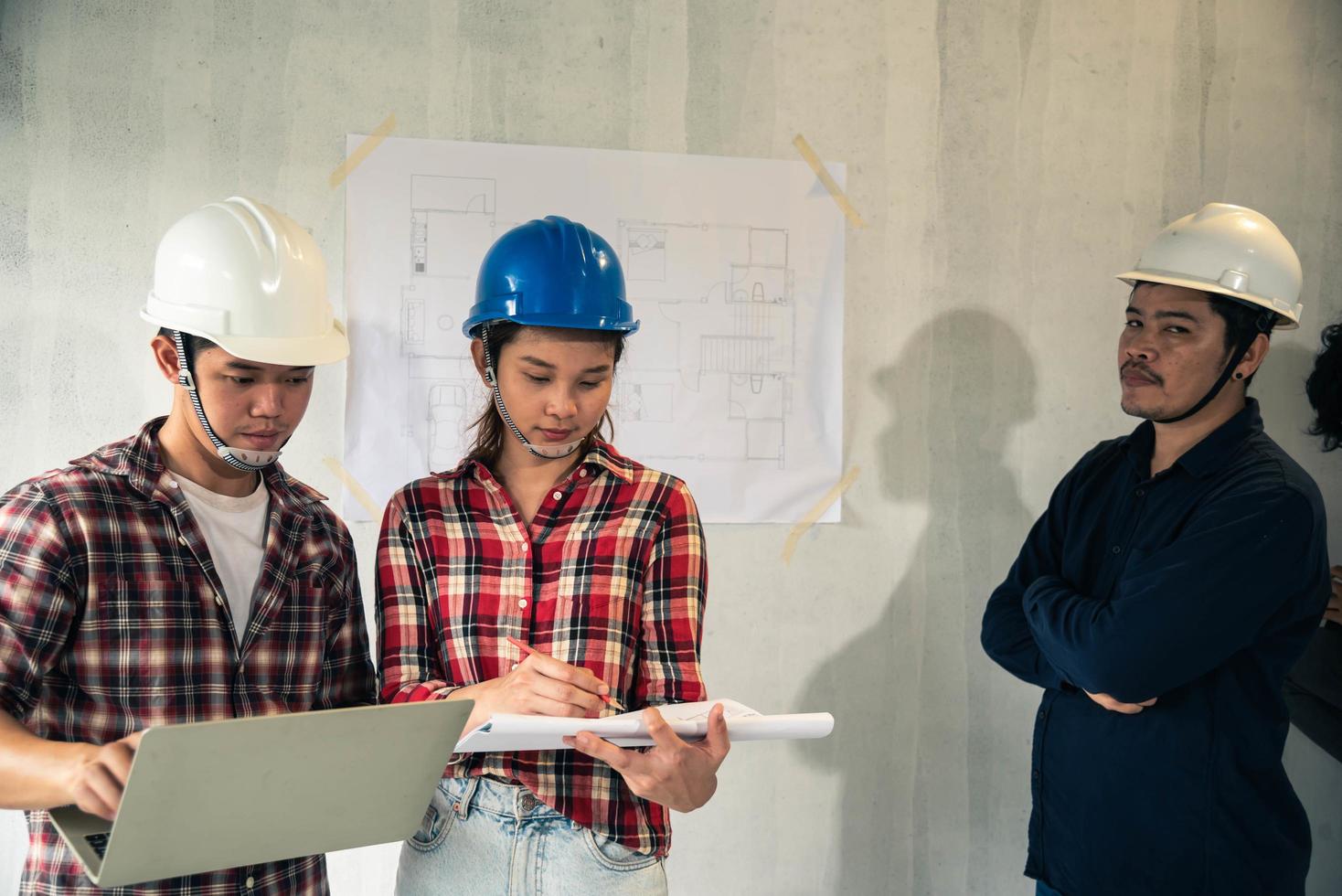 Joven pareja asiática en cascos examinando los planos de la casa con el ingeniero foto