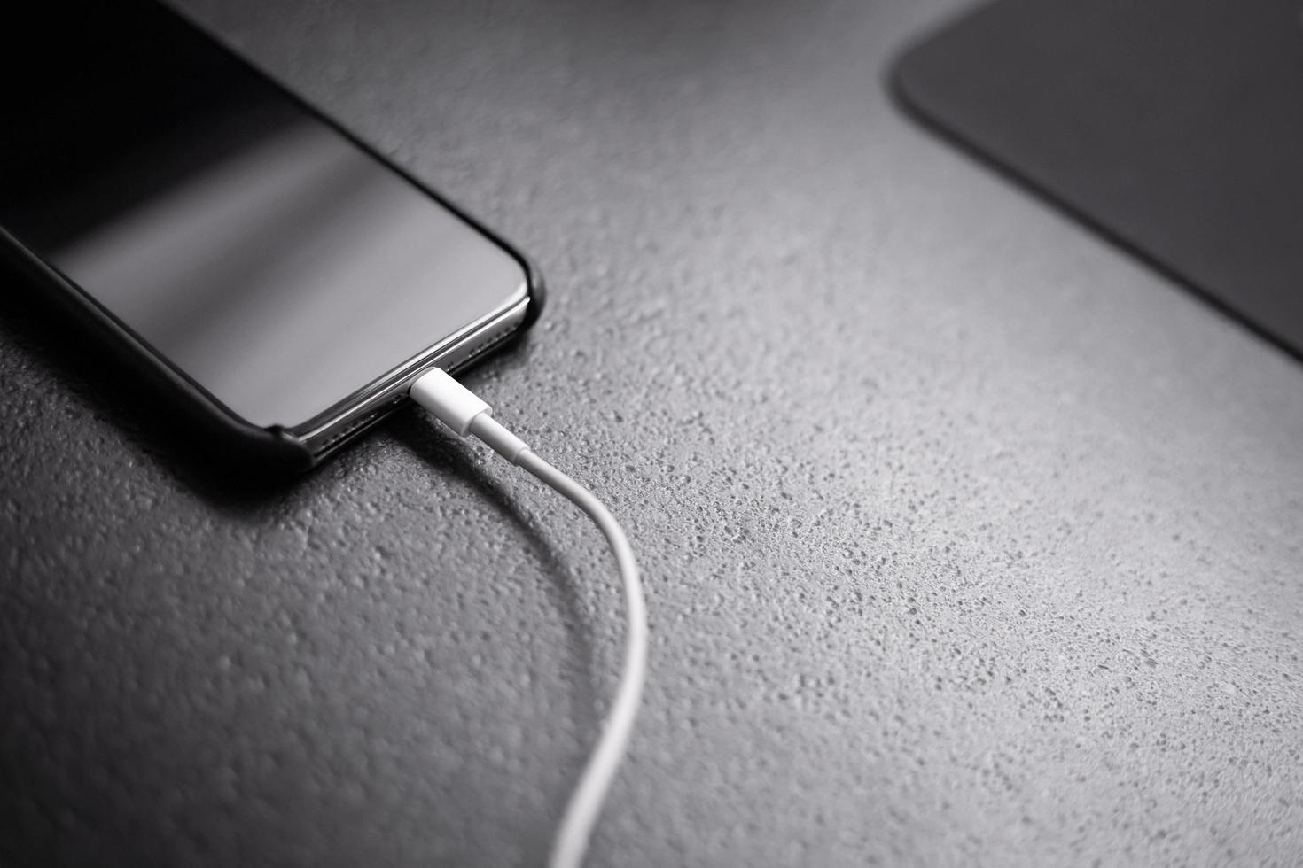 Cell phone connected to a charger next to a mousepad on a dark surface photo