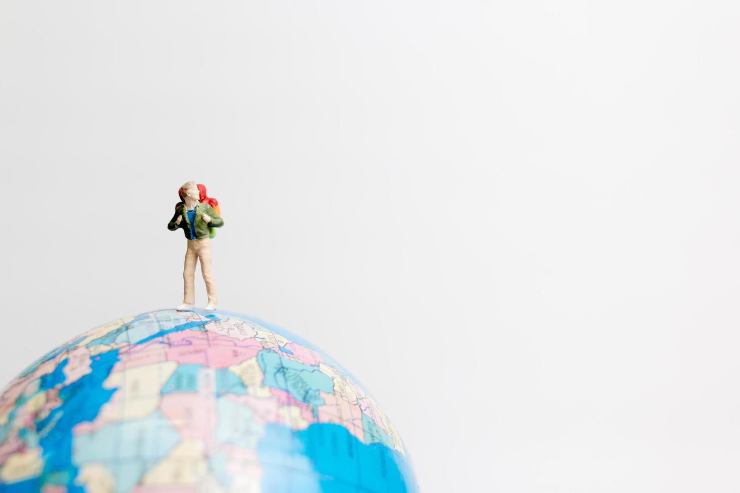 Persona en miniatura de pie sobre un globo terráqueo con un fondo blanco, concepto de viaje foto