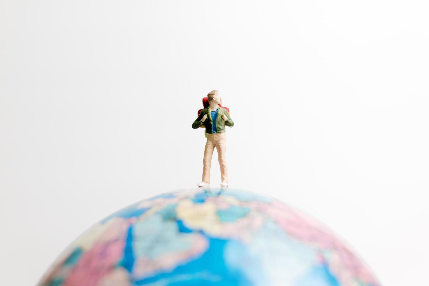 Miniature person standing on a globe with a white background, travel concept photo