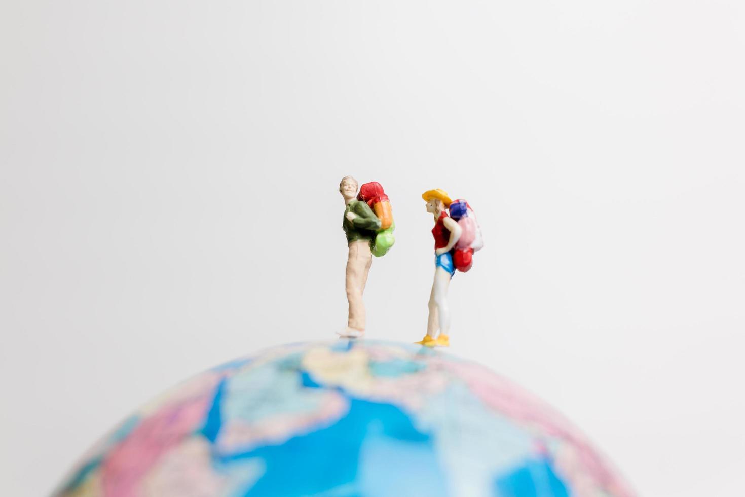 Gente en miniatura de pie sobre un globo terráqueo con un fondo blanco, concepto de viaje foto