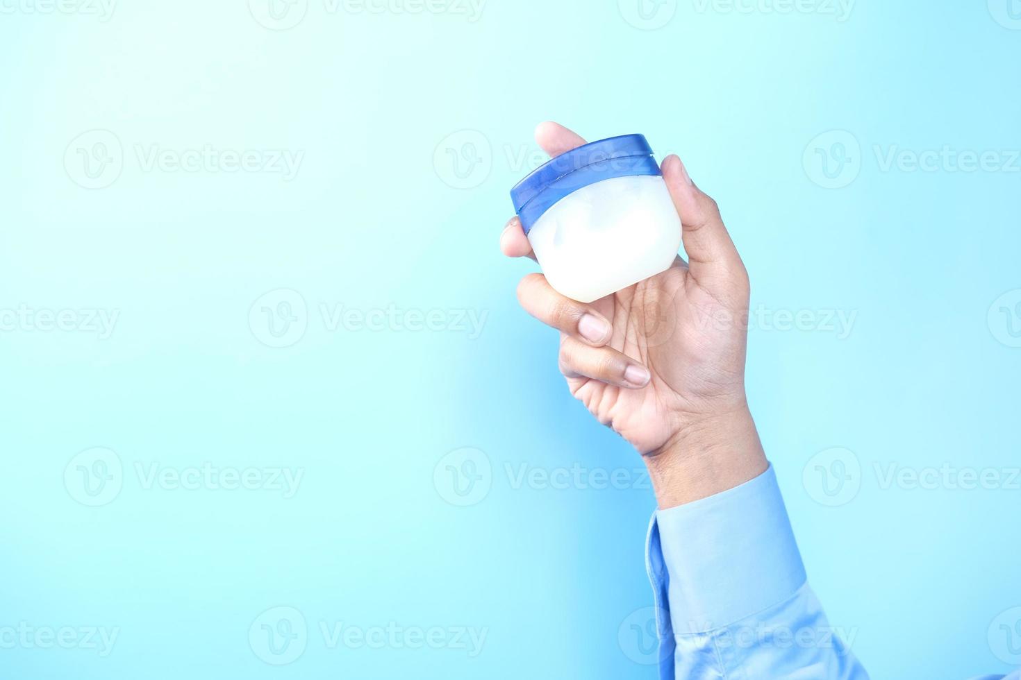 Hand holding petroleum jelly against blue background photo