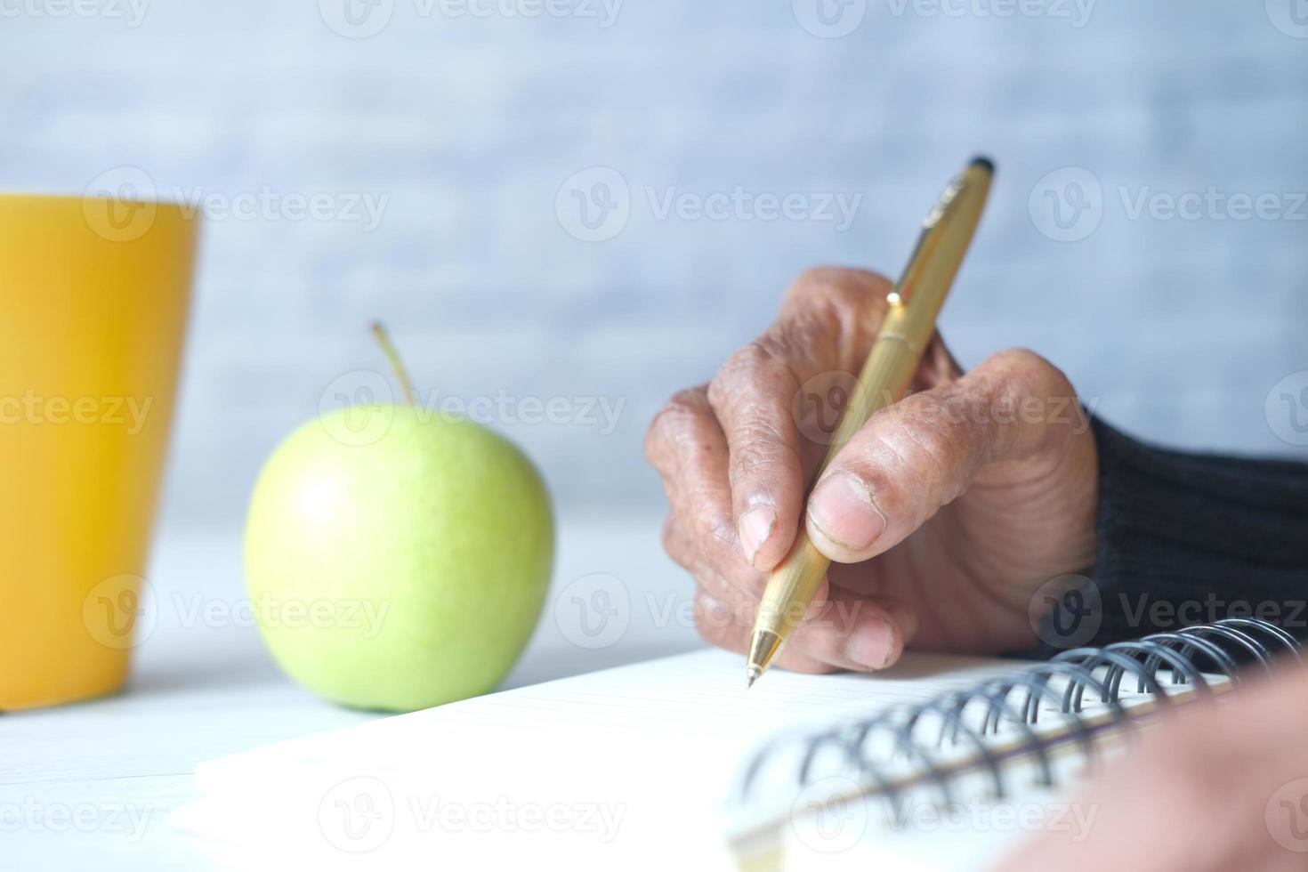 Cerca de la mano de la mujer mayor escribiendo en el bloc de notas foto