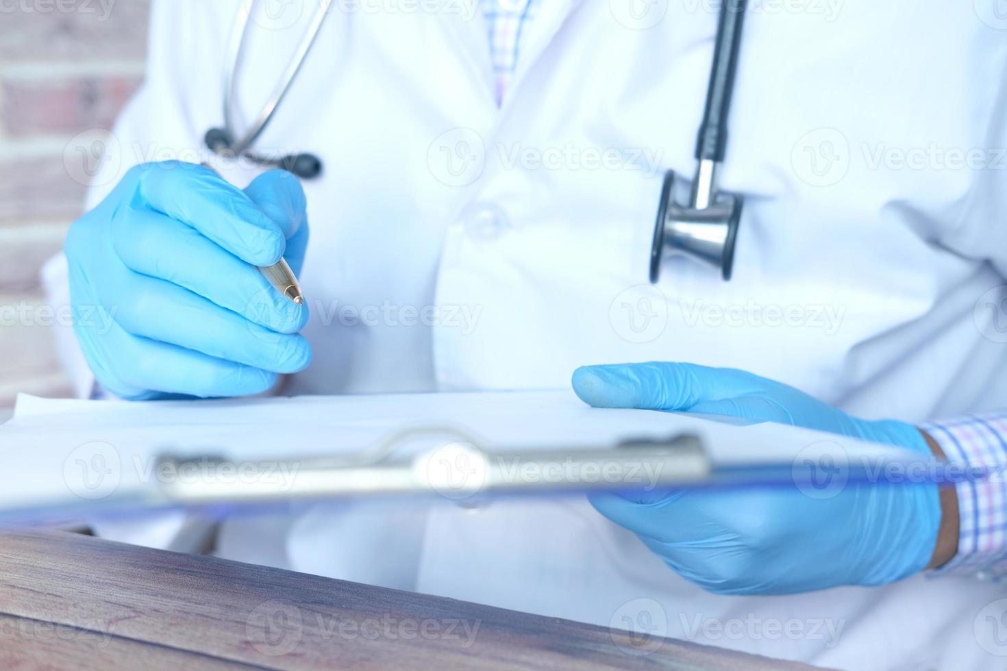 Doctor's hand in latex gloves writing prescription on desk photo