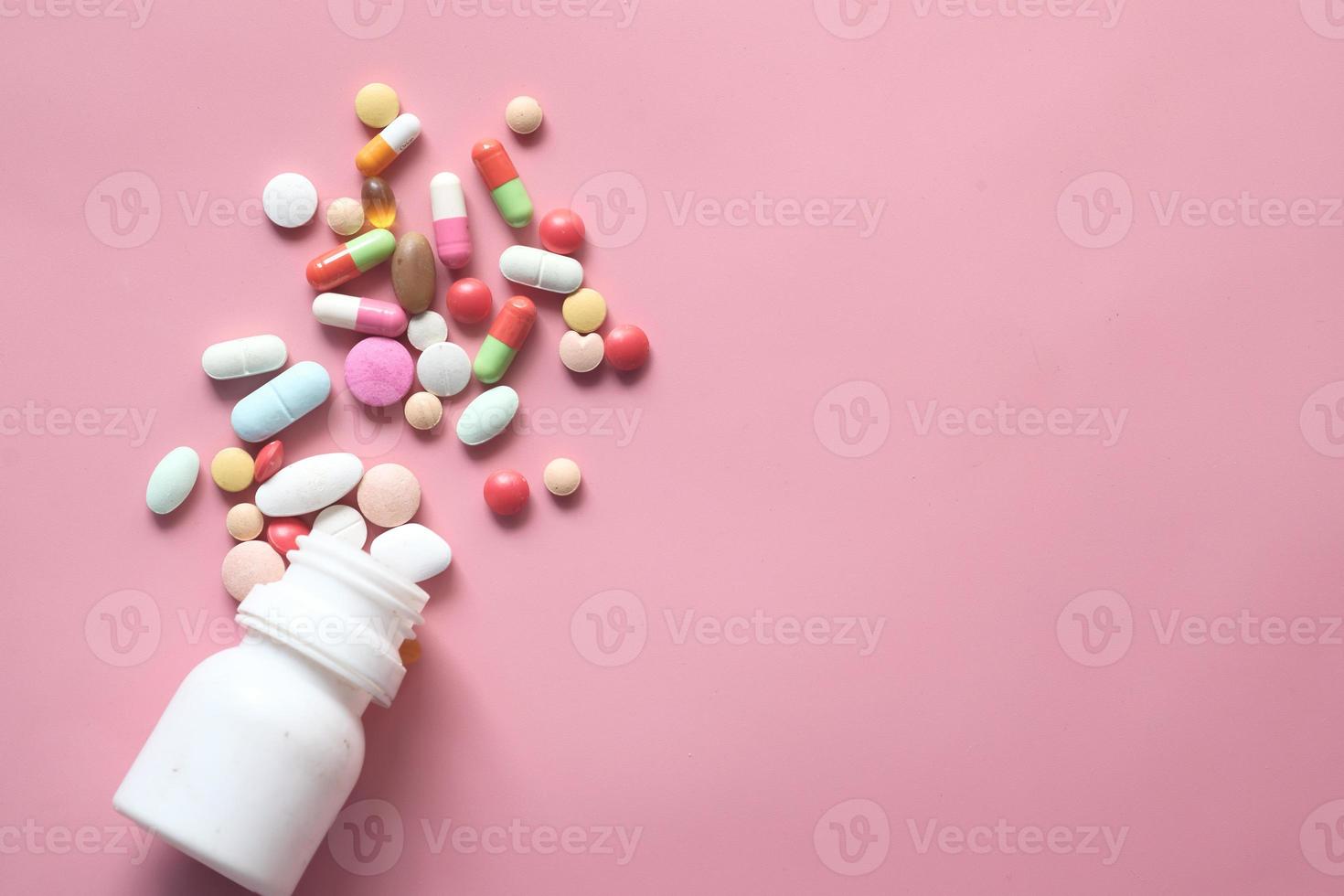 Colorful pills and capsules spilling on pink background photo