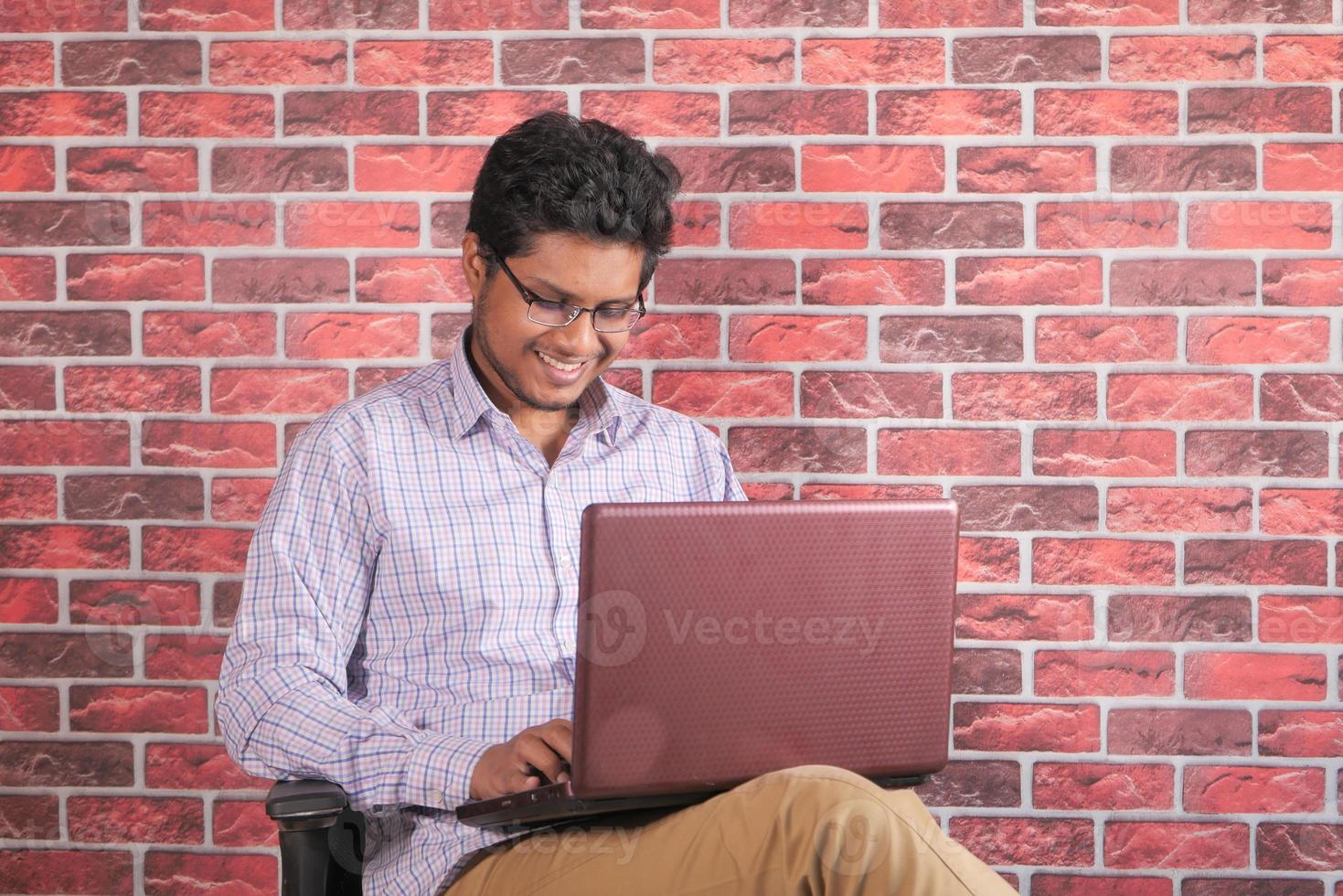 joven, usar la computadora portátil, mientras, sentado, en, un, silla foto