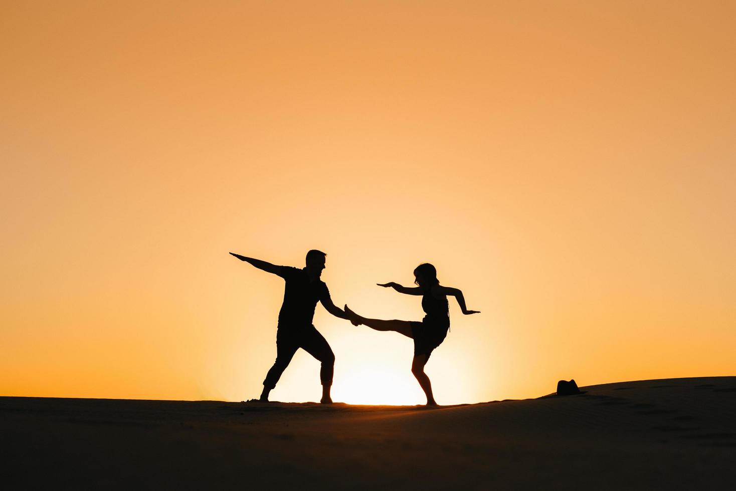 Siluetas de una joven pareja feliz sobre un fondo de naranja atardecer en el desierto de arena foto