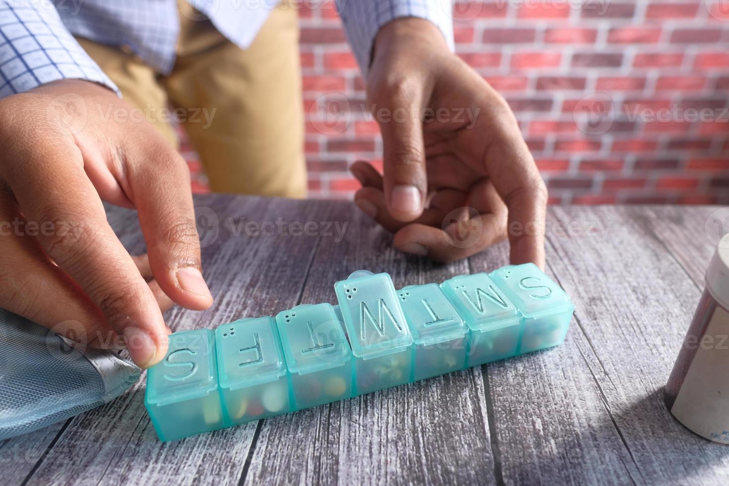 Las manos del hombre tomando medicamentos de un organizador de pastillas. foto