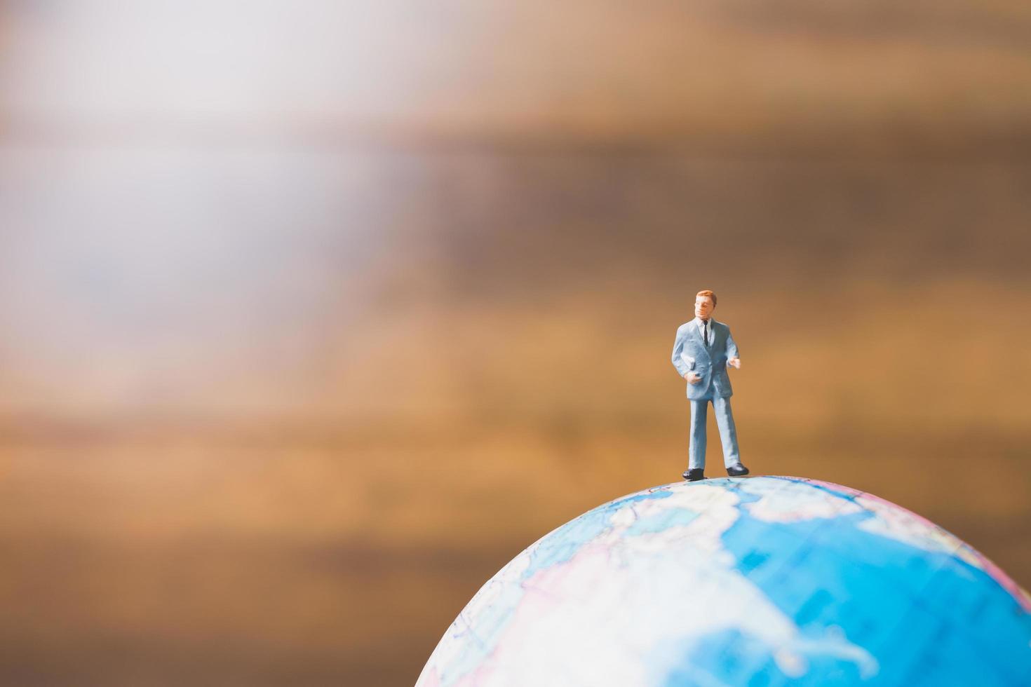 Miniature businessman standing on a globe world map with a brown background photo