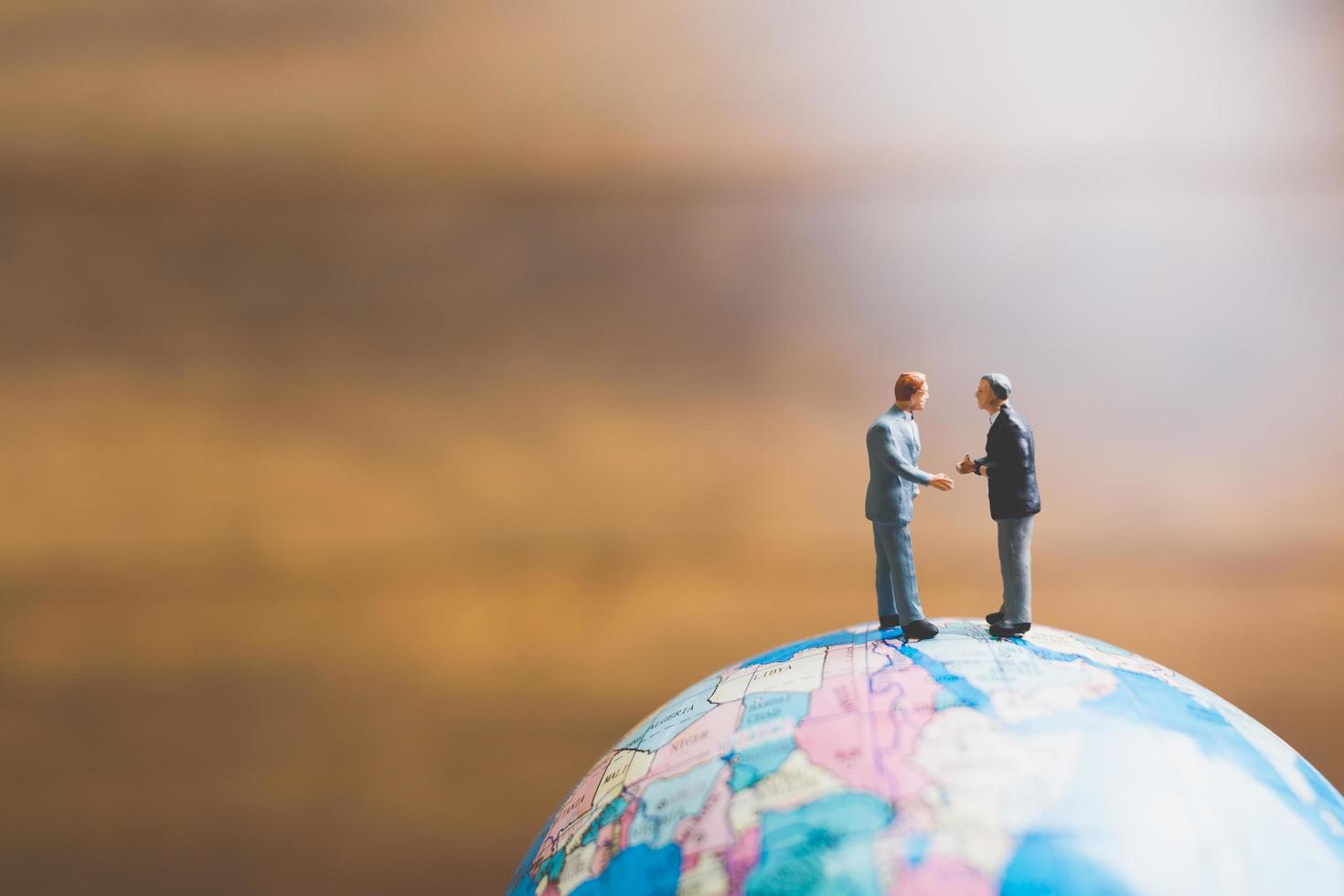 Miniature businessmen standing on a globe world map with a brown background photo