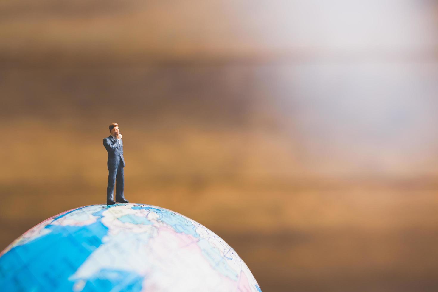 Miniature businessman standing on a globe world map with a brown background photo