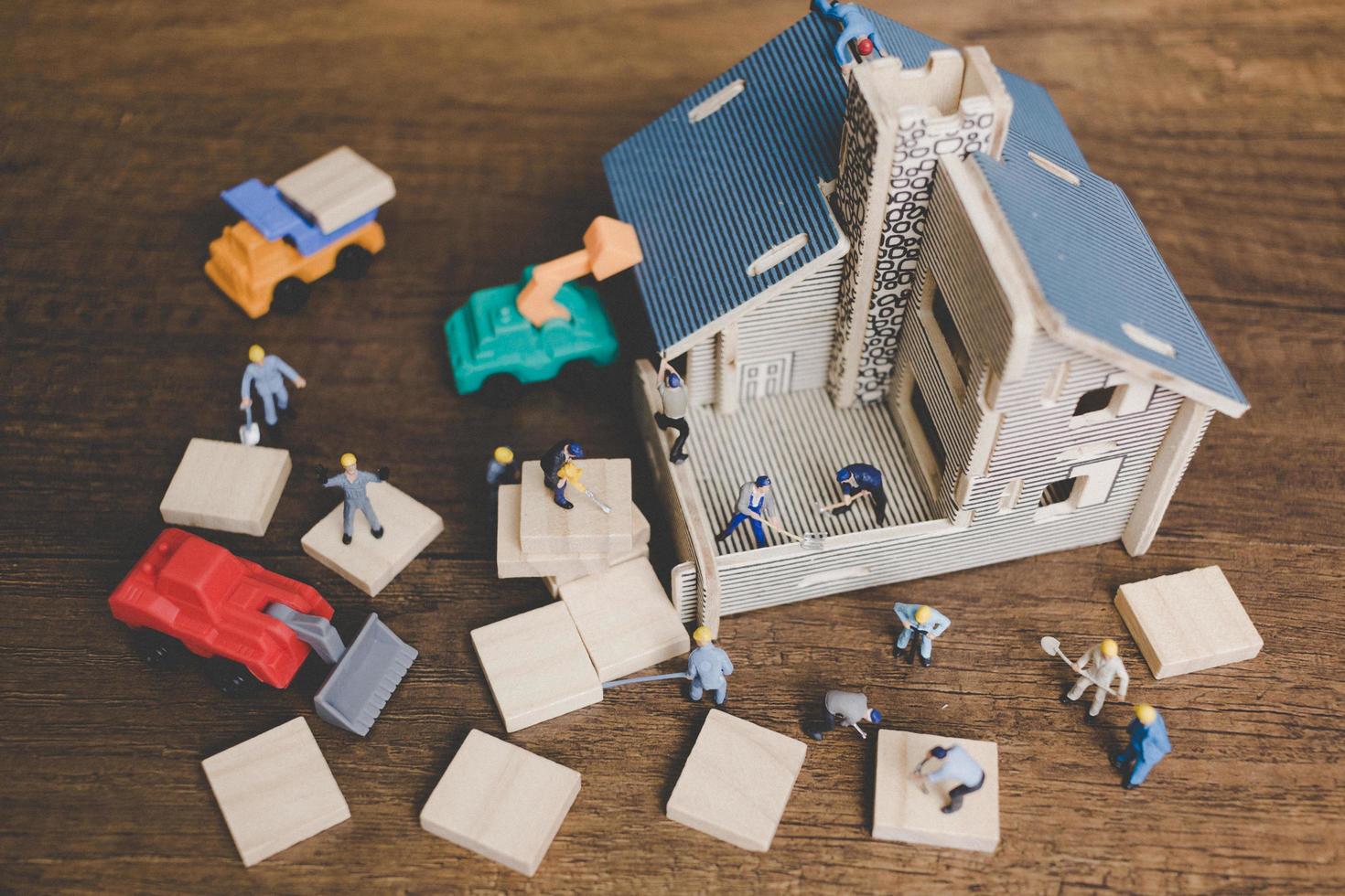 Miniature workers repairing a house on a wooden background photo