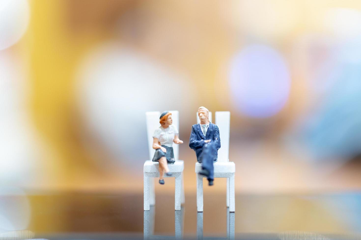 Miniature businesspeople sitting on chairs with a colorful bokeh background photo