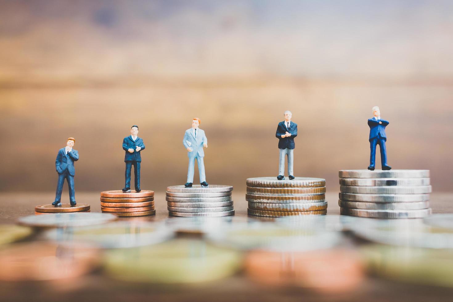 Miniature businesspeople standing on money with a wooden background photo