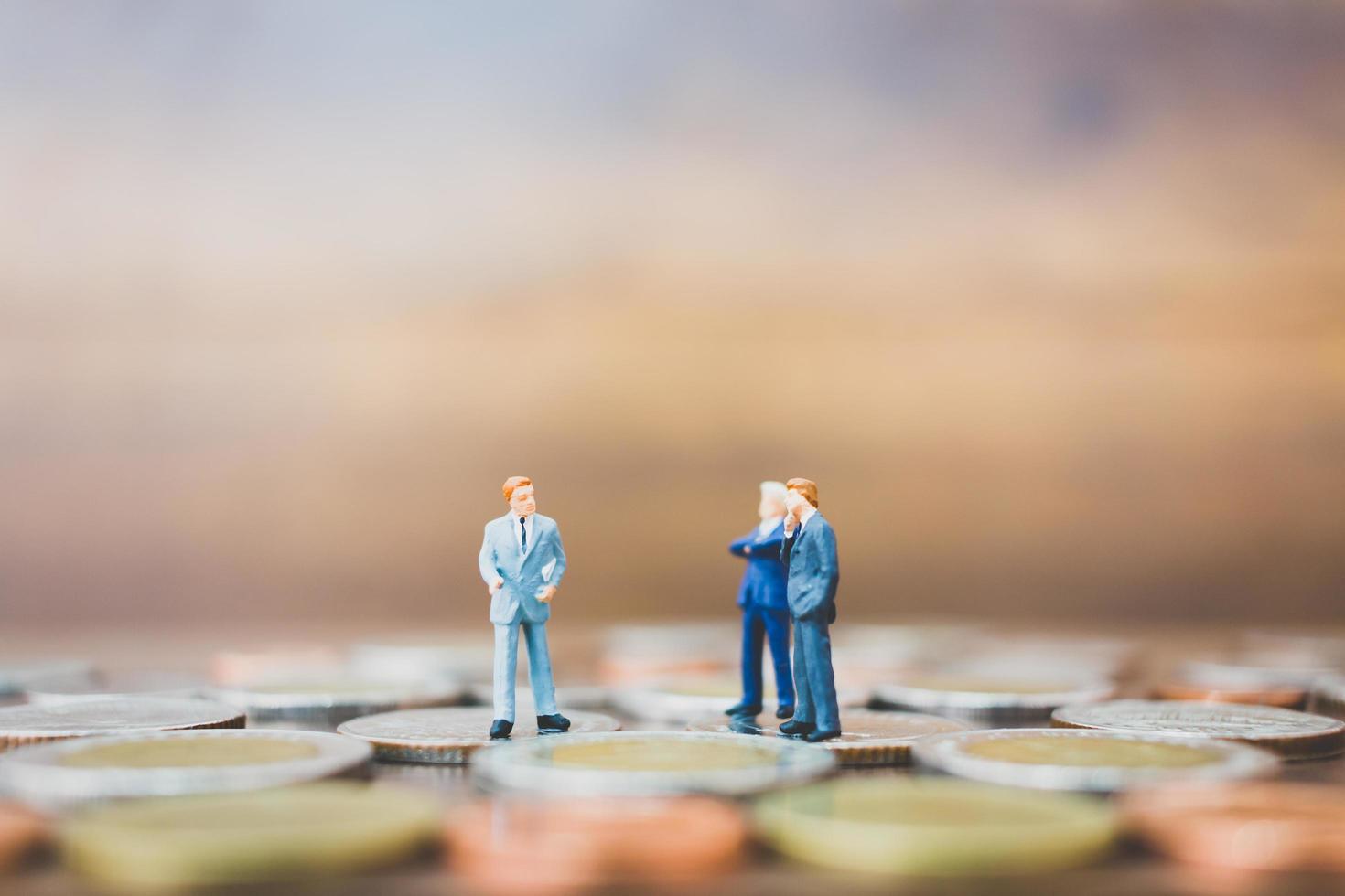 Miniature businesspeople standing on money with a wooden background photo