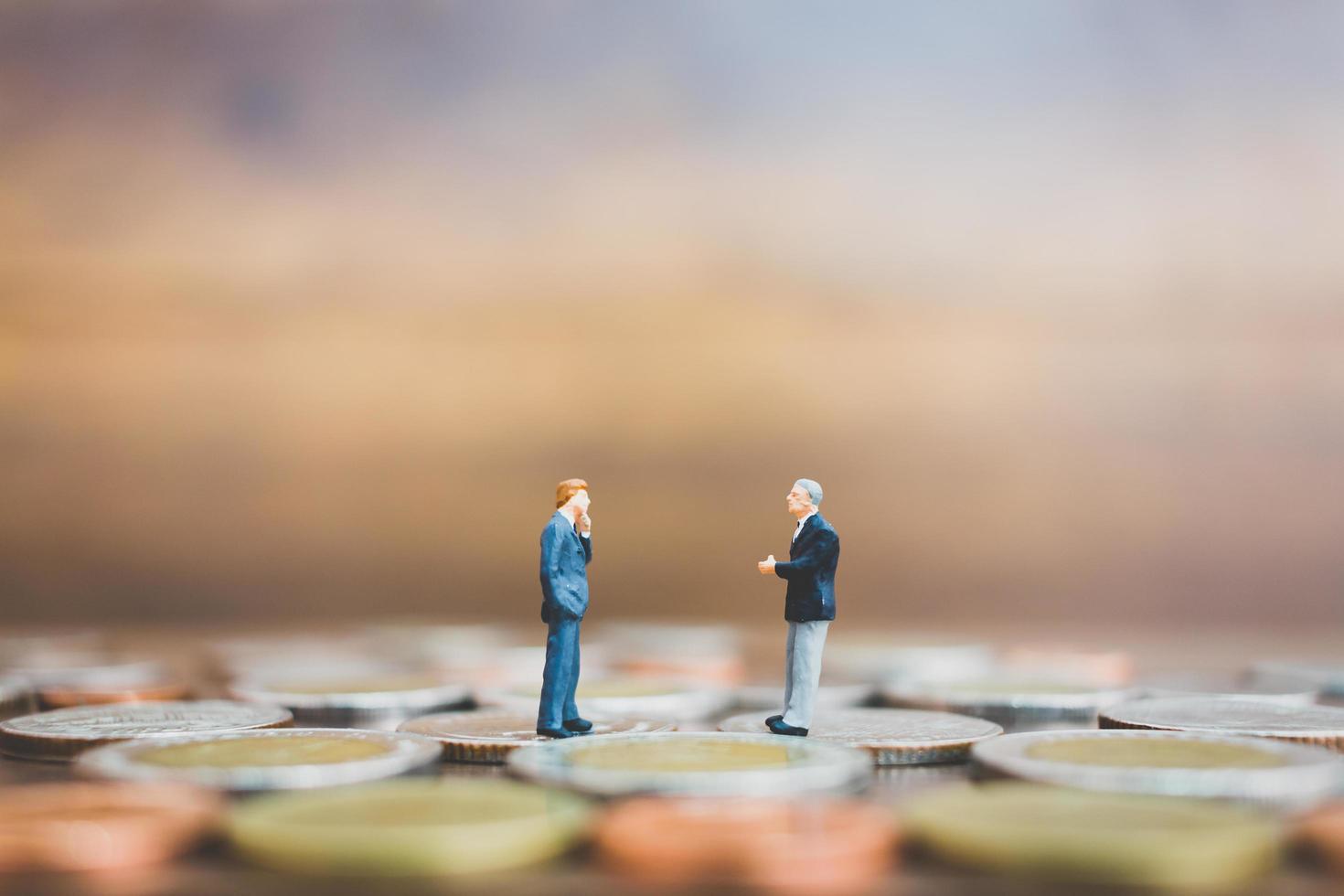 Miniature businesspeople standing on money with a wooden background photo