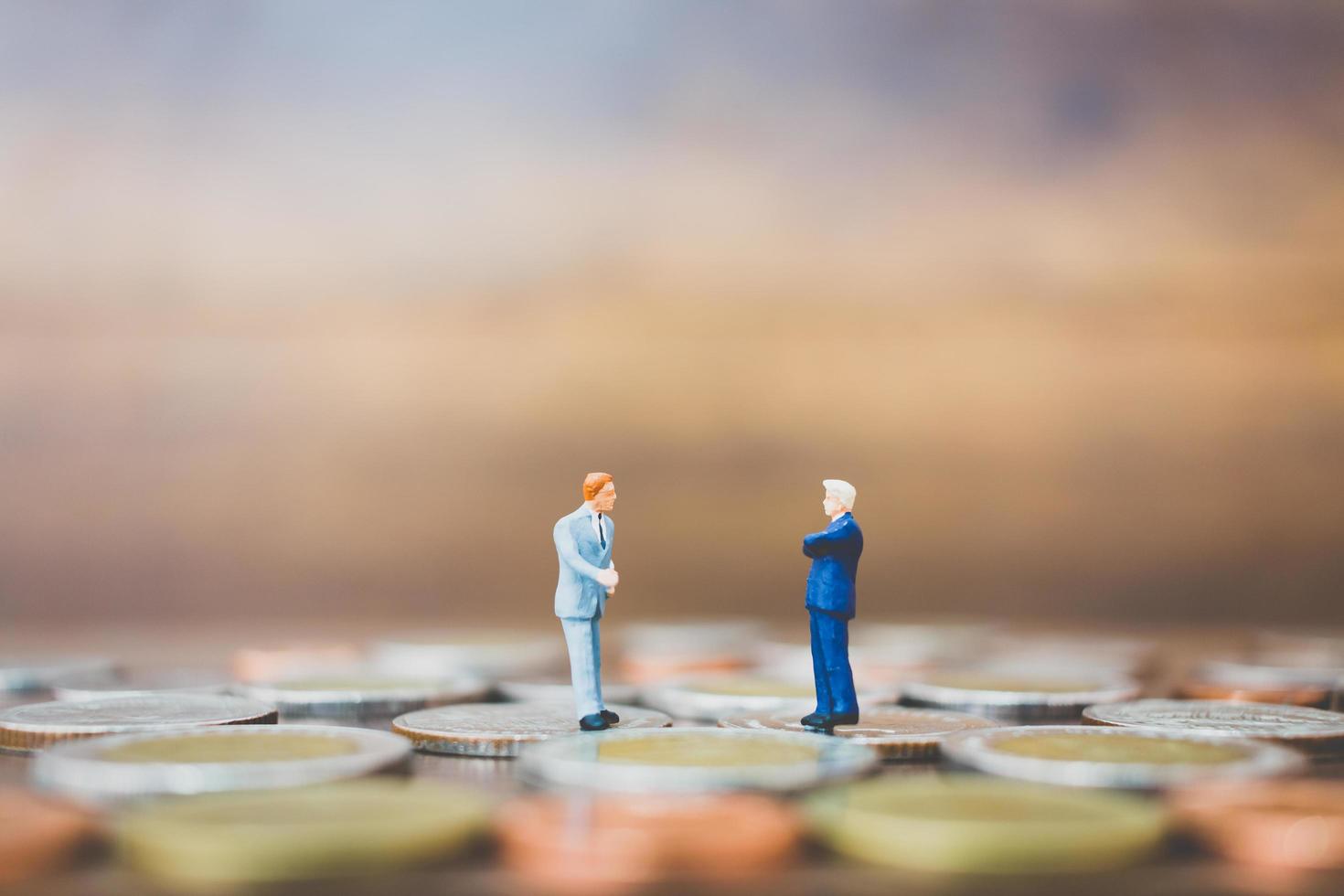 Miniature businesspeople standing on money with a wooden background photo