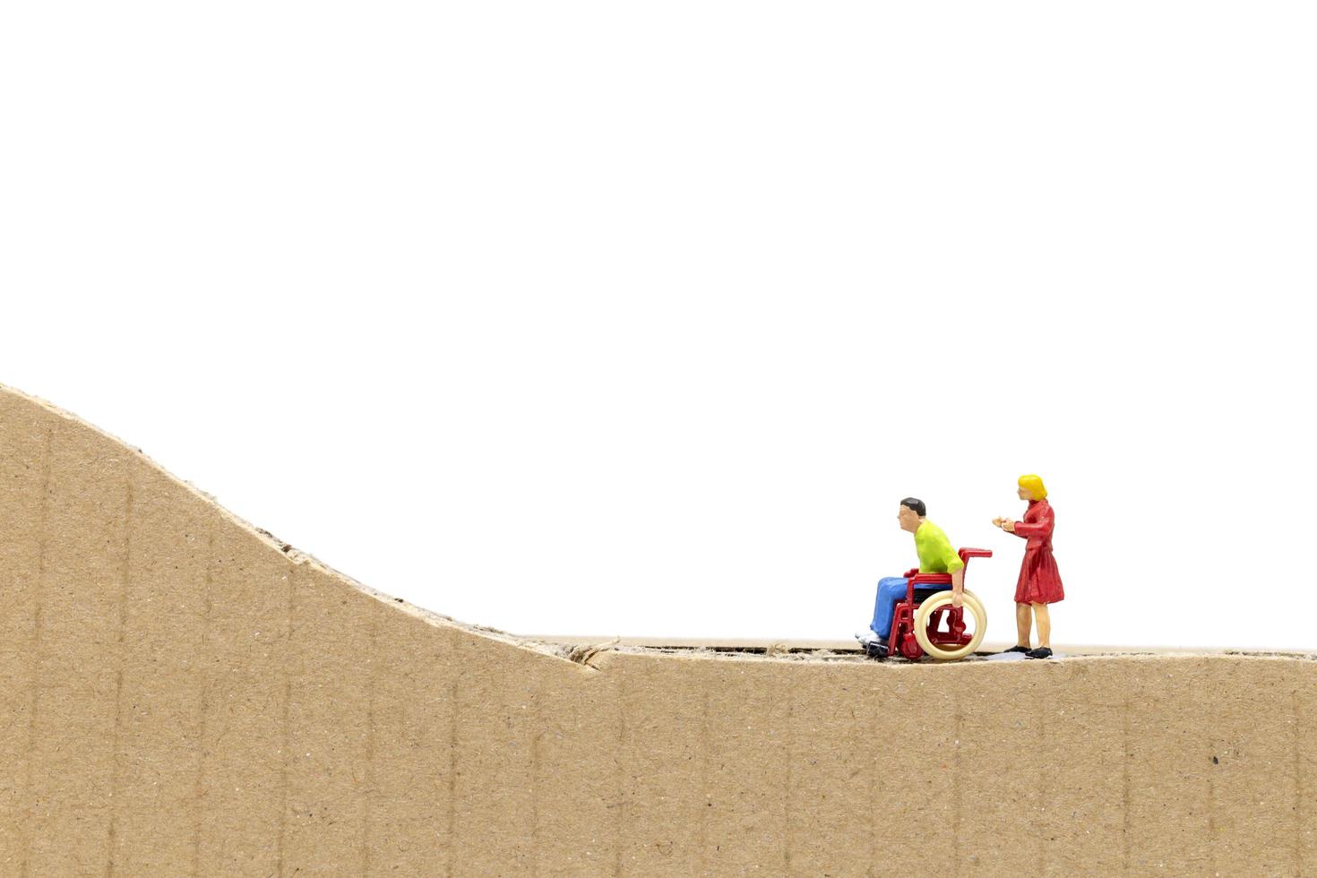 Miniature man in a wheelchair and woman on a cardboard cutout isolated on a white background photo