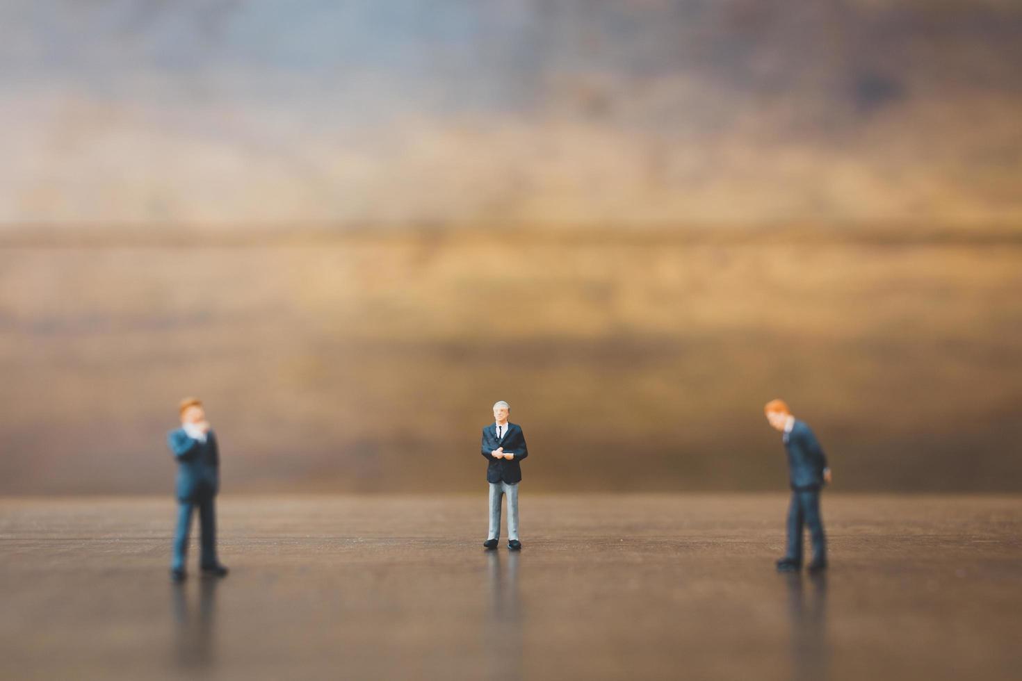 Miniature businesspeople standing on a wooden background photo
