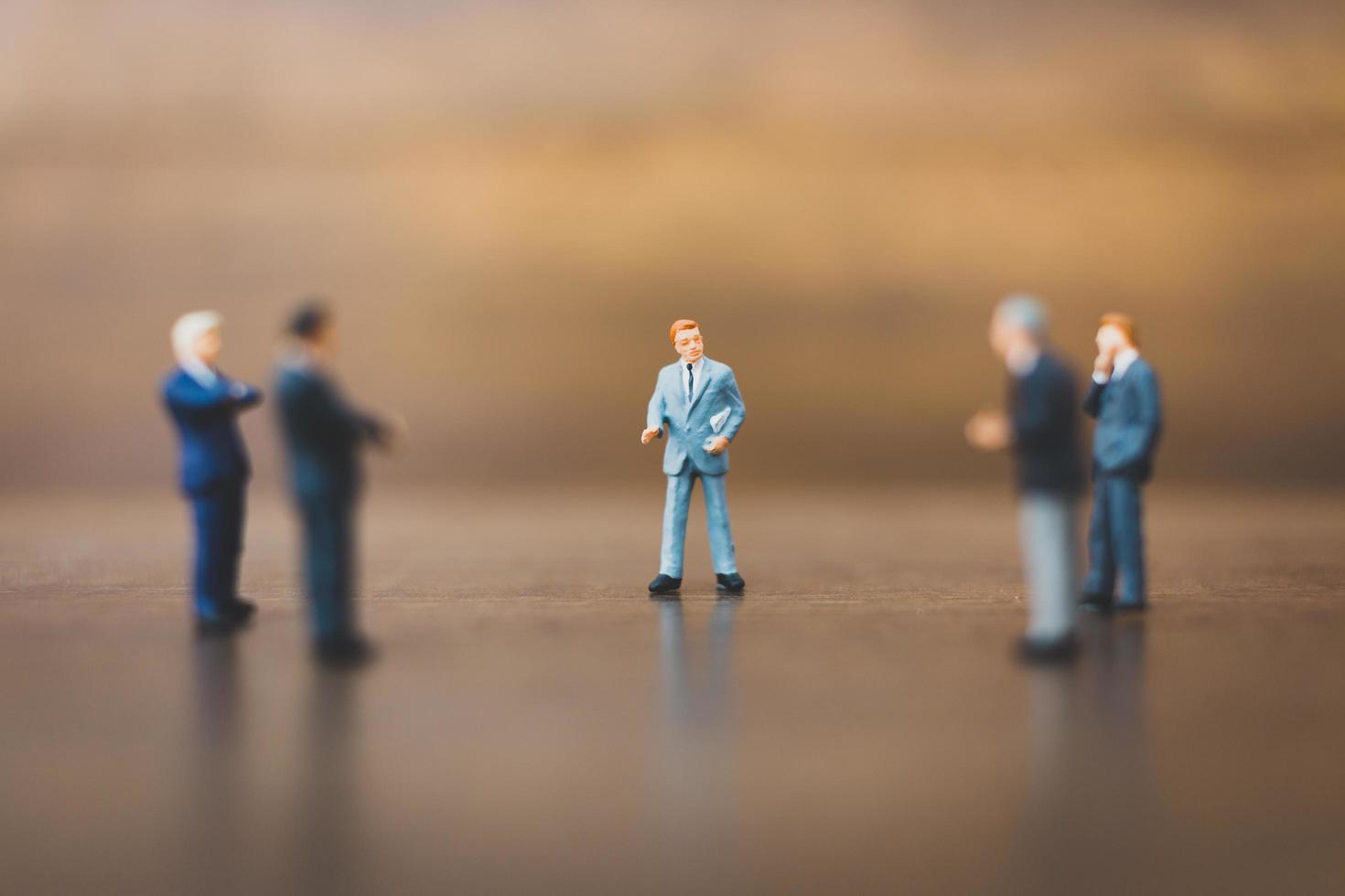 Miniature businesspeople standing on a wooden background photo