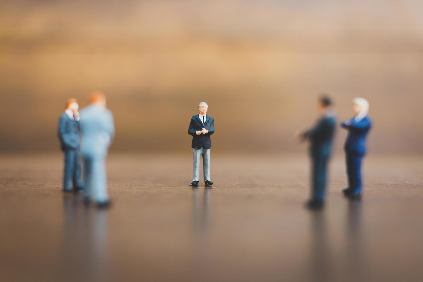 Miniature businesspeople standing on a wooden background photo