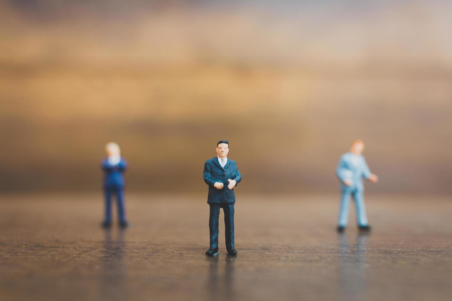 Miniature businesspeople standing on a wooden background photo