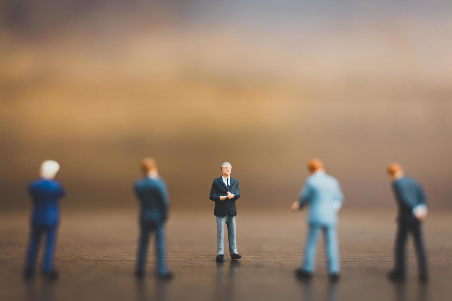 Miniature businesspeople standing on a wooden background photo