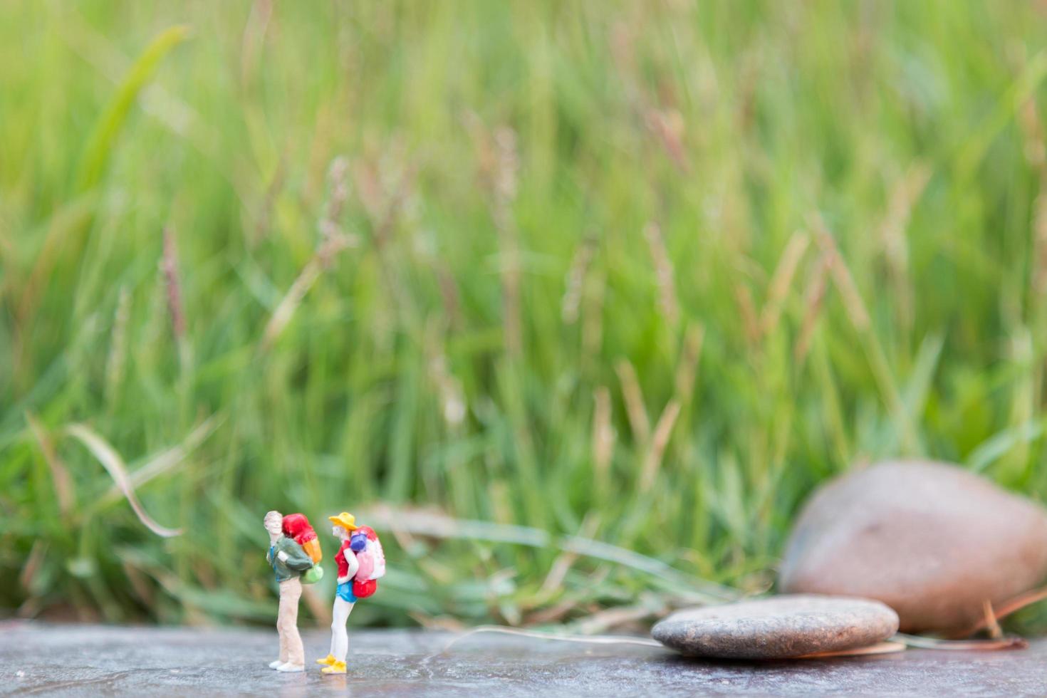 Viajeros en miniatura con mochilas de pie y caminando en un prado foto