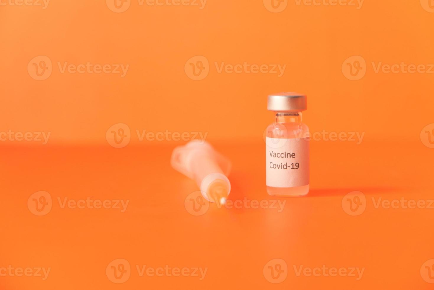 Close up of coronavirus vaccine and syringe on orange background photo
