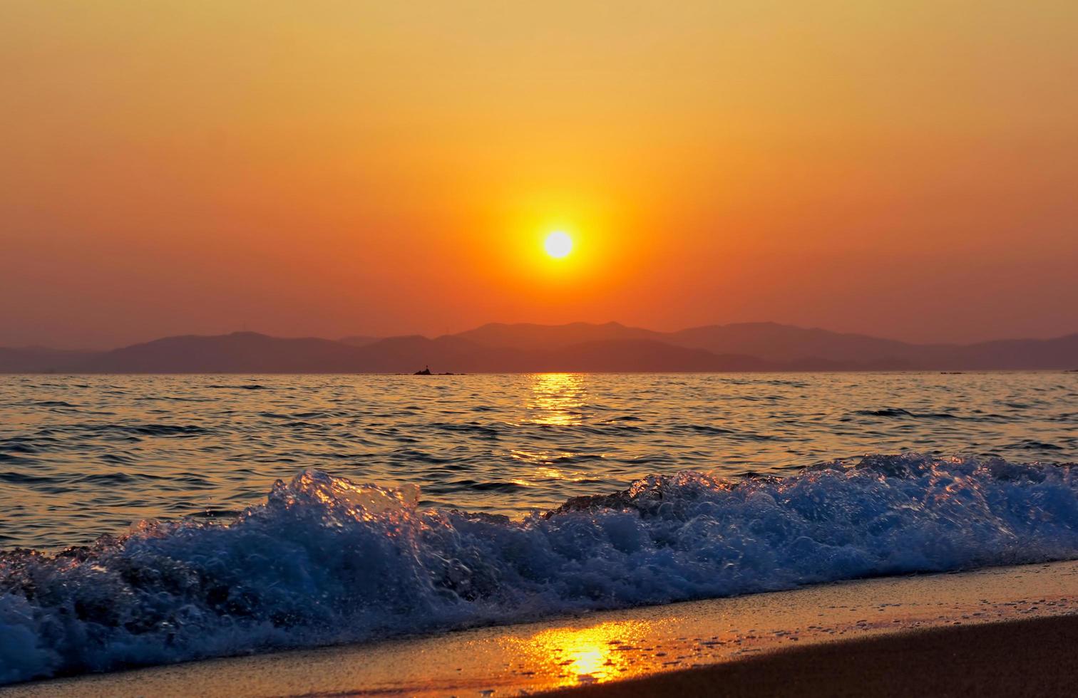 Olas rompiendo en una playa con atardecer nublado naranja sobre las montañas foto