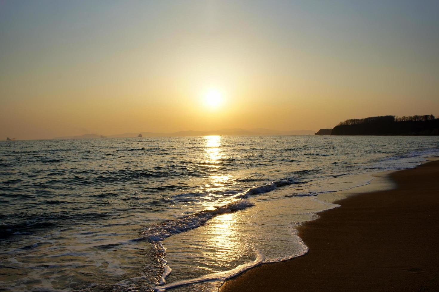 puesta de sol sobre las montañas y el cuerpo de agua en una playa foto