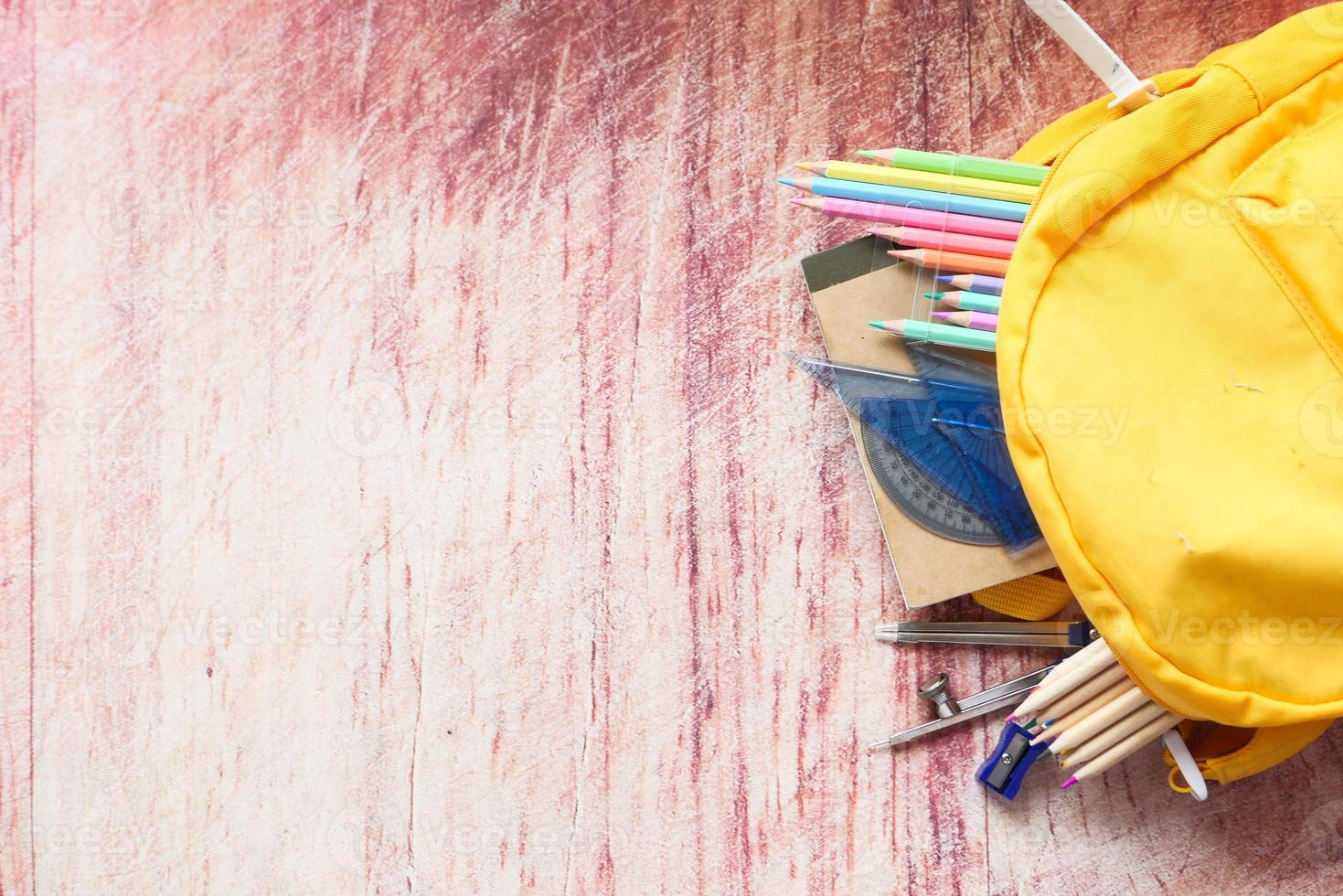 Top view of yellow backpack with different colorful stationery on table photo