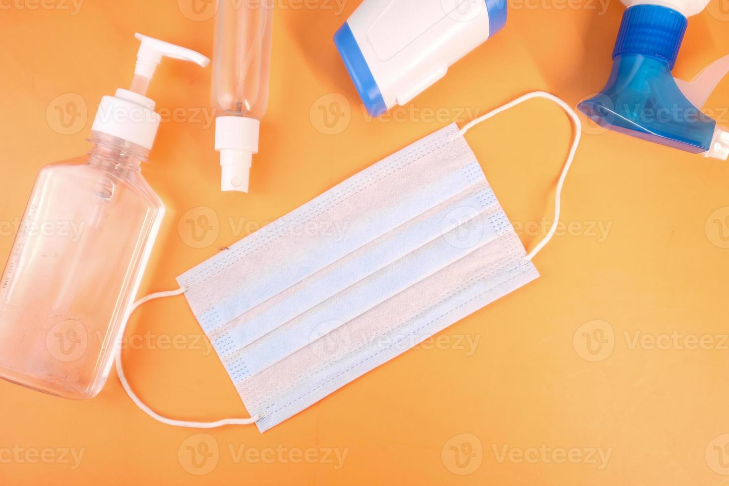 Surgical masks, thermometer, and hand sanitizer on orange background photo