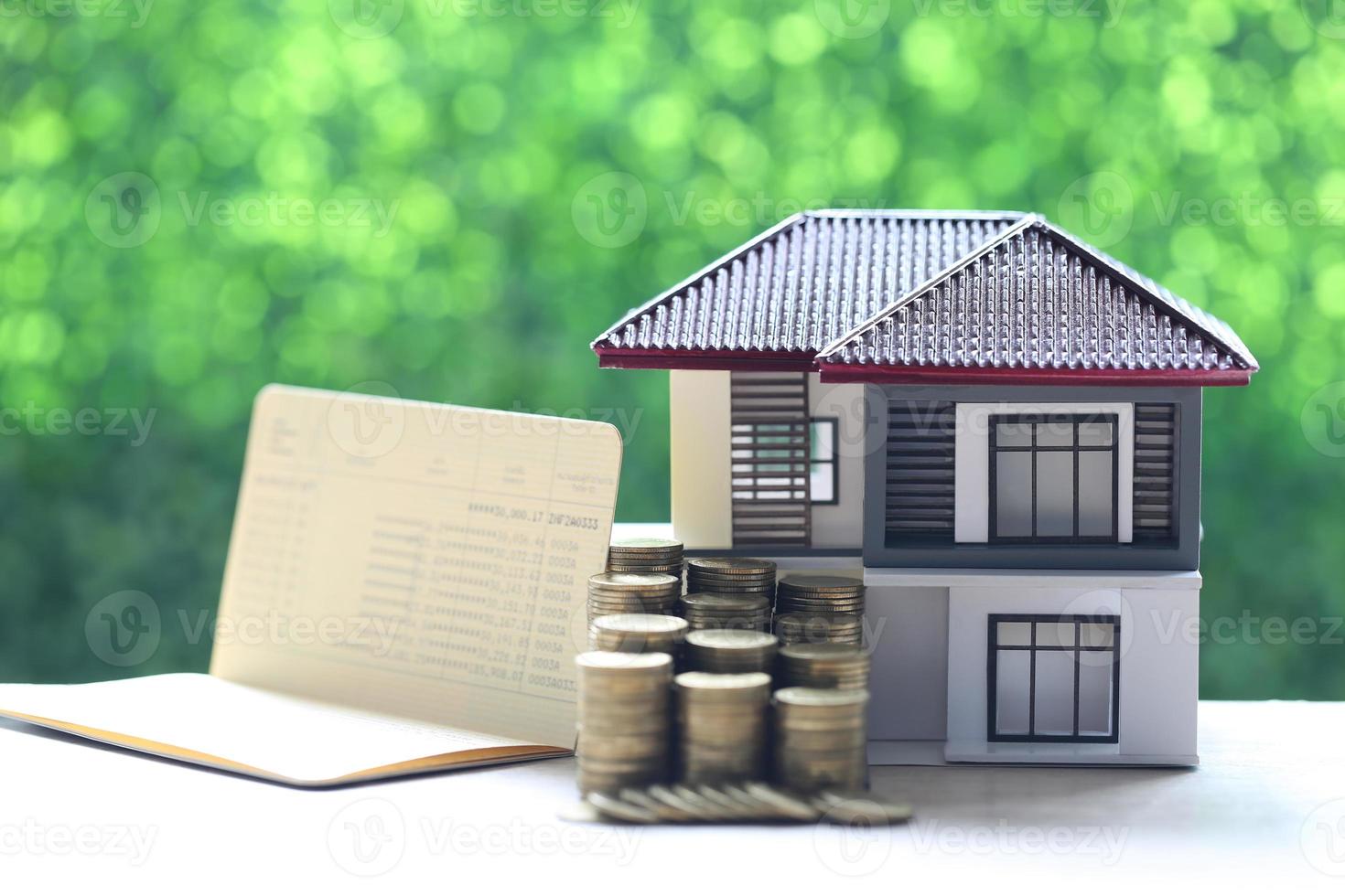 Model house and a stack of coins with a banking account book on a natural green background, business investment and real estate concept photo
