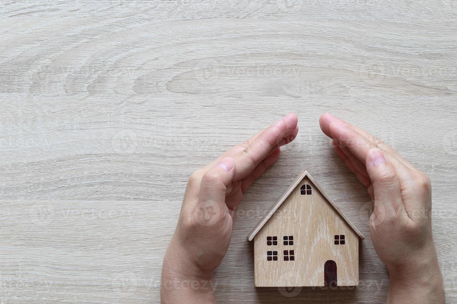 Hand protecting a model house on a wooden background, finance insurance and safe investment concept photo