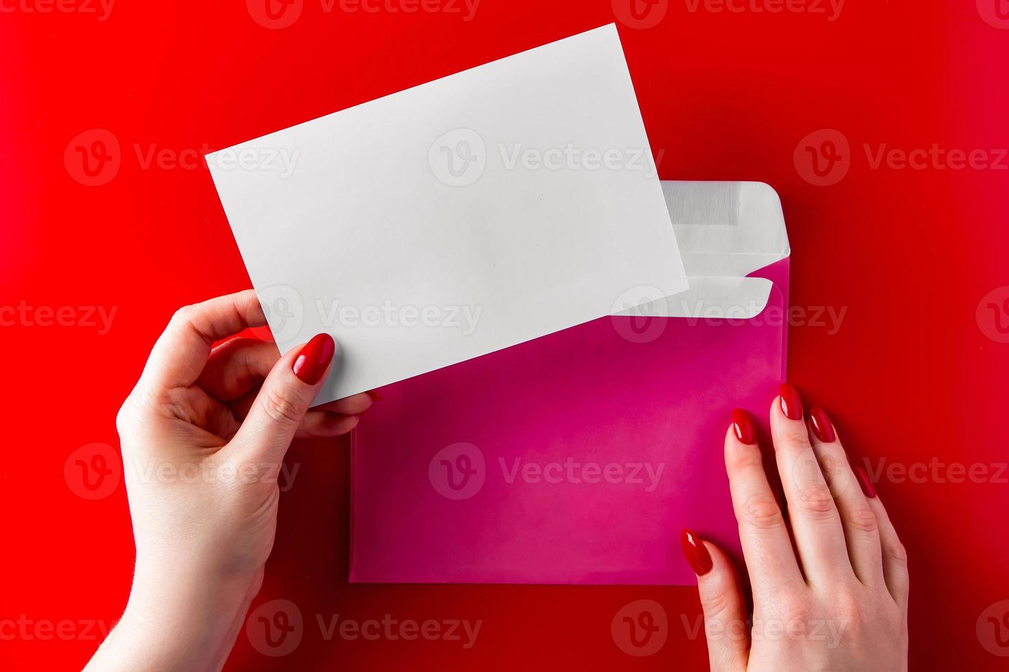Un sobre de felicitación en manos de una mujer joven sobre un fondo rojo. foto