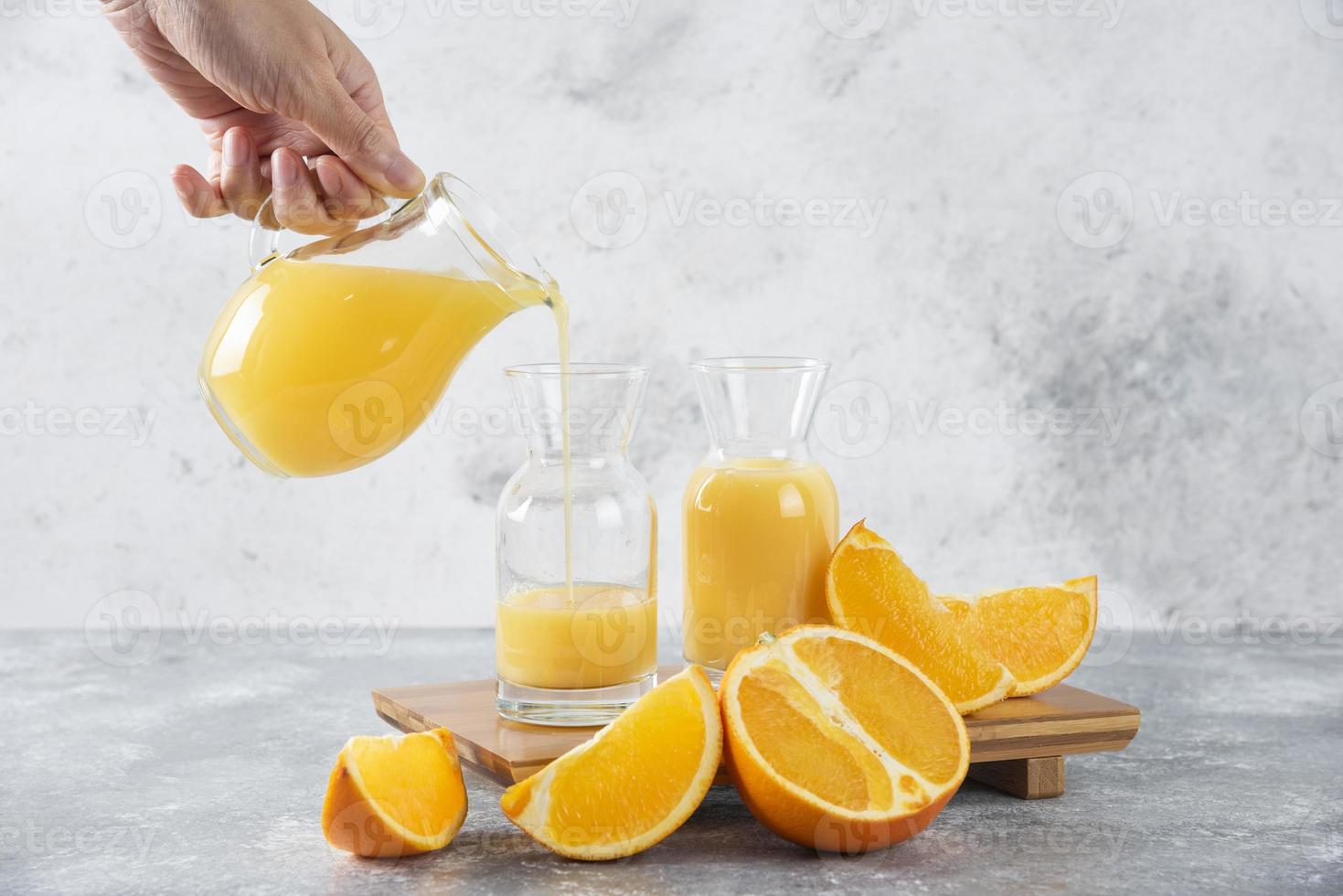 Hand pouring fresh orange juice on a stone background photo