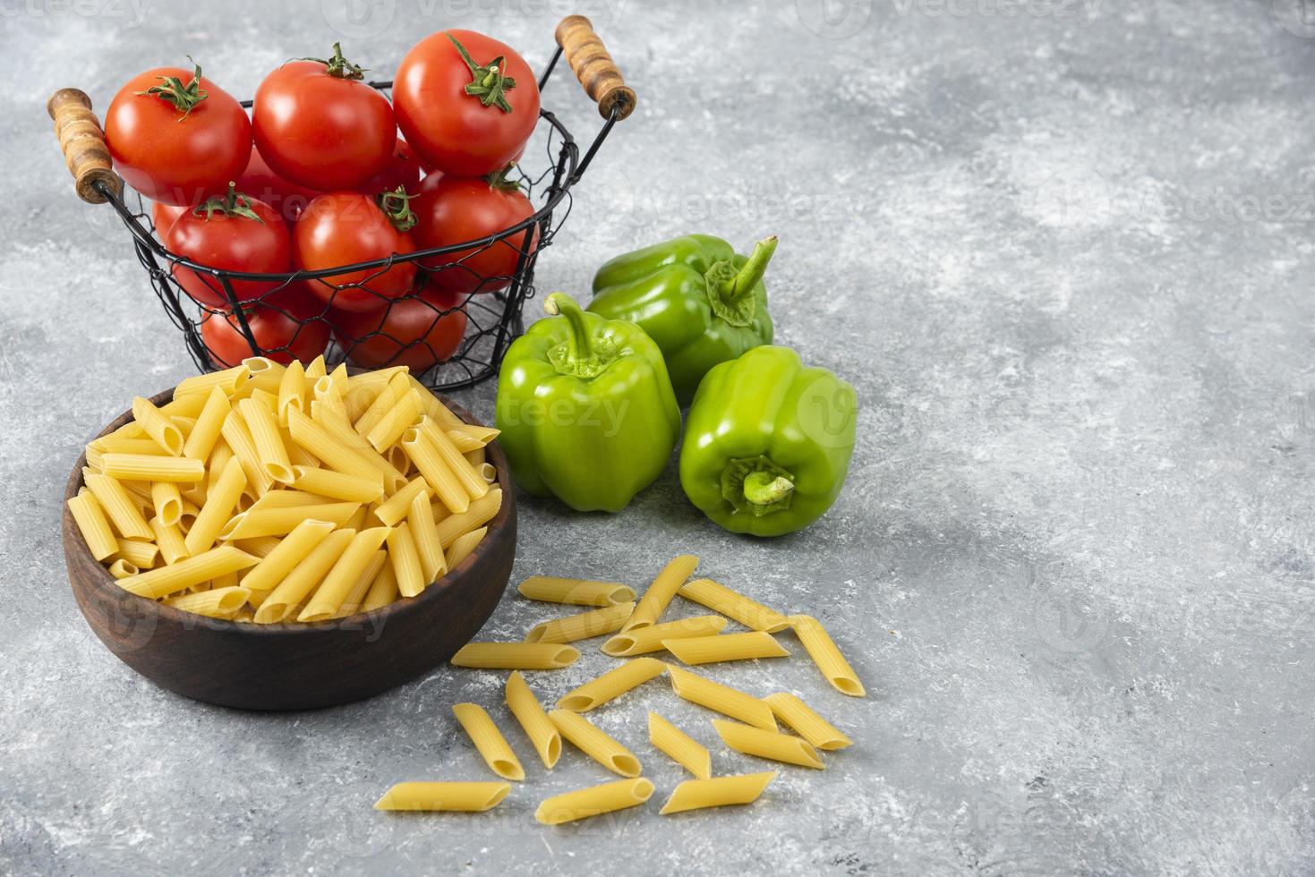 Pasta cruda con verduras frescas maduras colocadas sobre una mesa de piedra foto