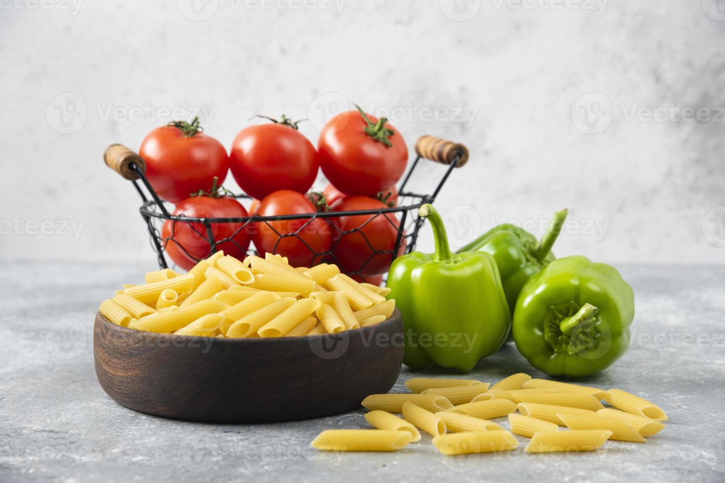 Uncooked pasta with fresh ripe vegetables placed on a stone table photo