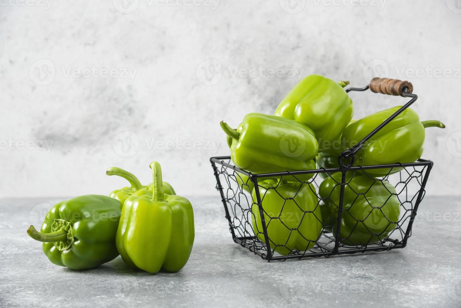 Fresh green bell peppers in a metallic basket placed on a stone background photo