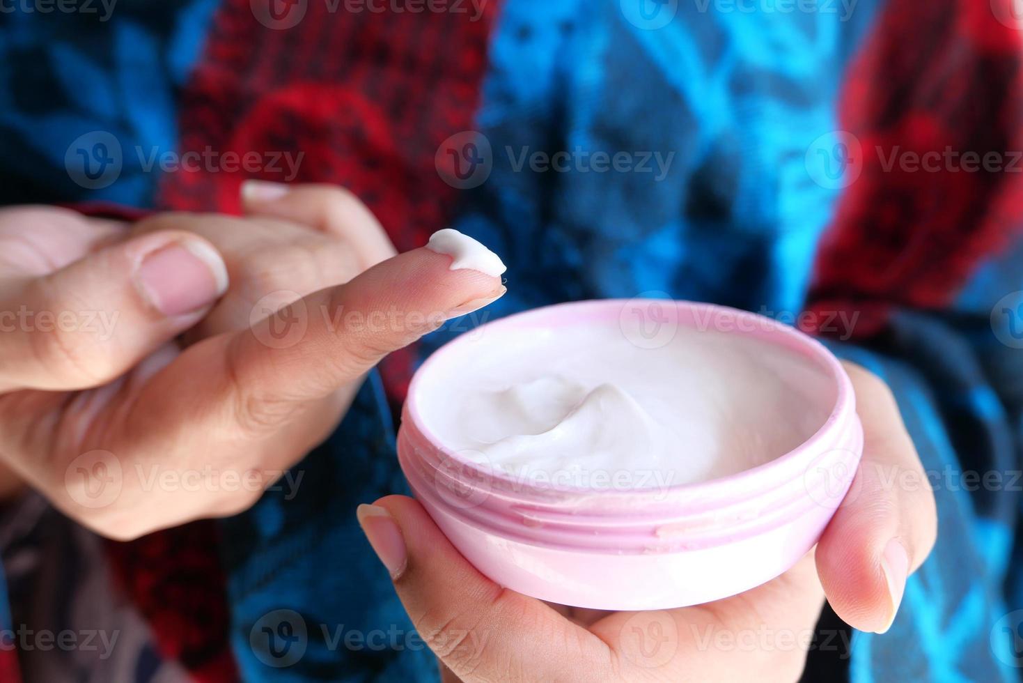 Person applying cream in pink container photo