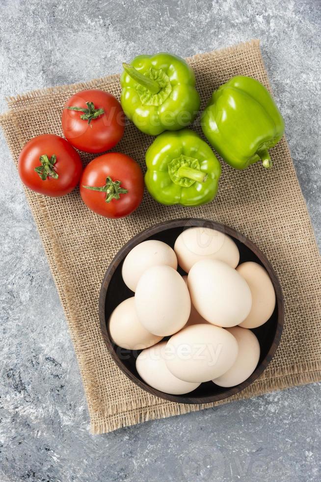 Recipiente de madera lleno de huevos de gallina cruda con verduras frescas maduras en un cilicio foto