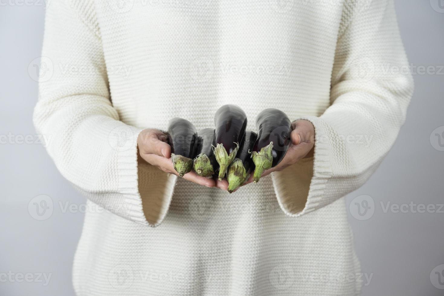 Manos femeninas sosteniendo verduras berenjenas maduras contra una pared gris foto