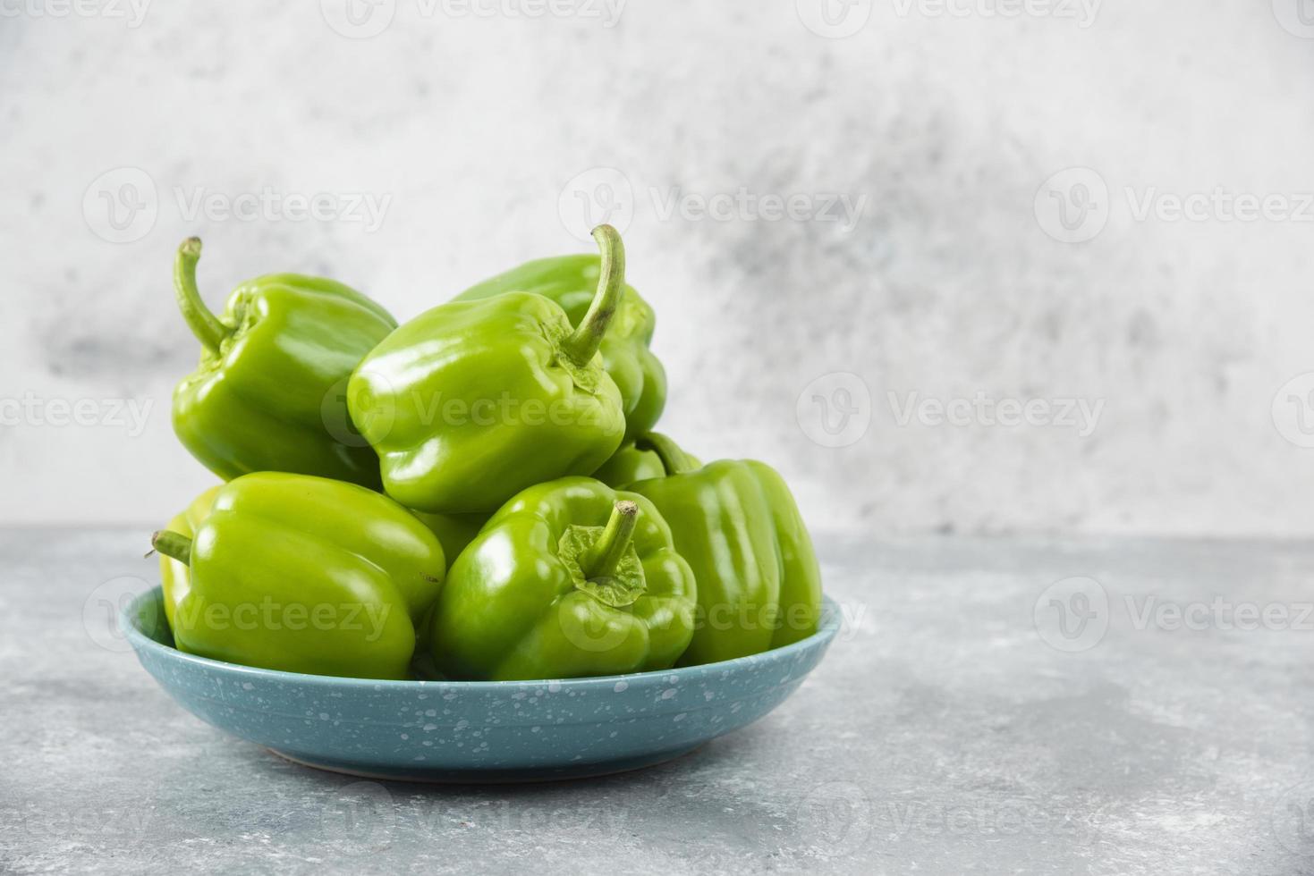 Pimientos verdes frescos colocados en una placa azul sobre una mesa de piedra foto