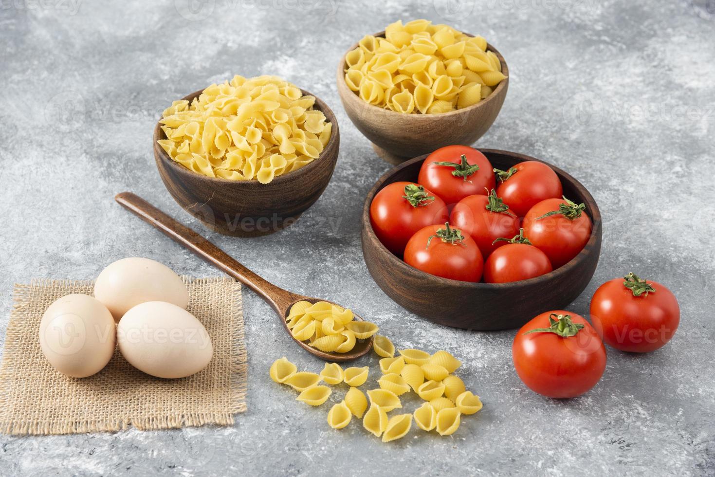 dos tipos de pasta cruda con huevos de gallina crudos y tomates rojos foto